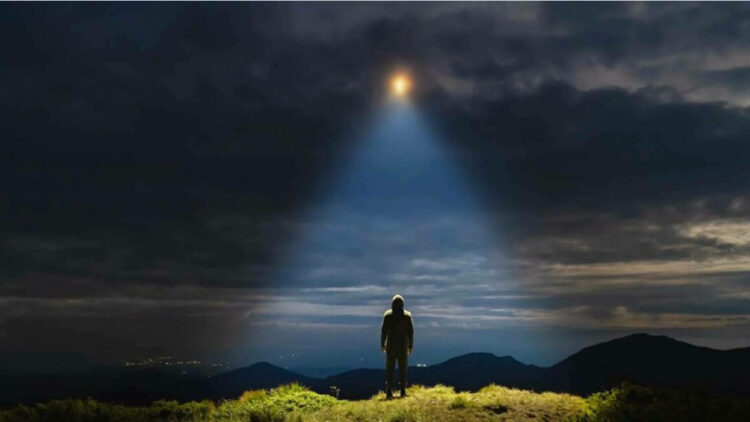 man looking to light in sky, grass, clouds, night
